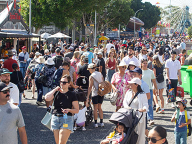 A large crowd moves along a busy showground walkway near rides and stalls at the Sydney Royal Easter Show.